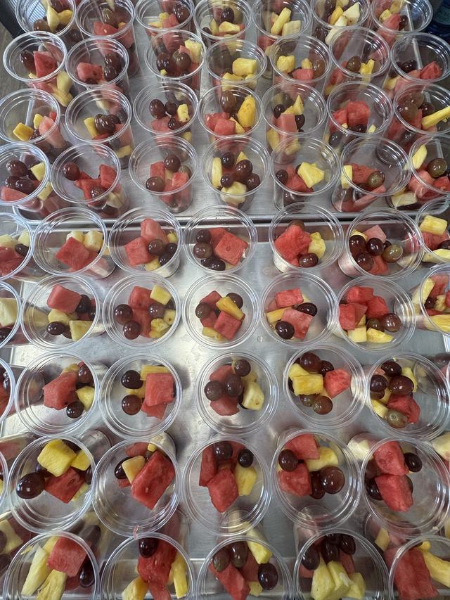 Sheet trays of fresh fruit cups with watermelon, pineapple and red grapes